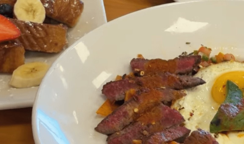 Sliced steak with a fried egg, French toast behind it.